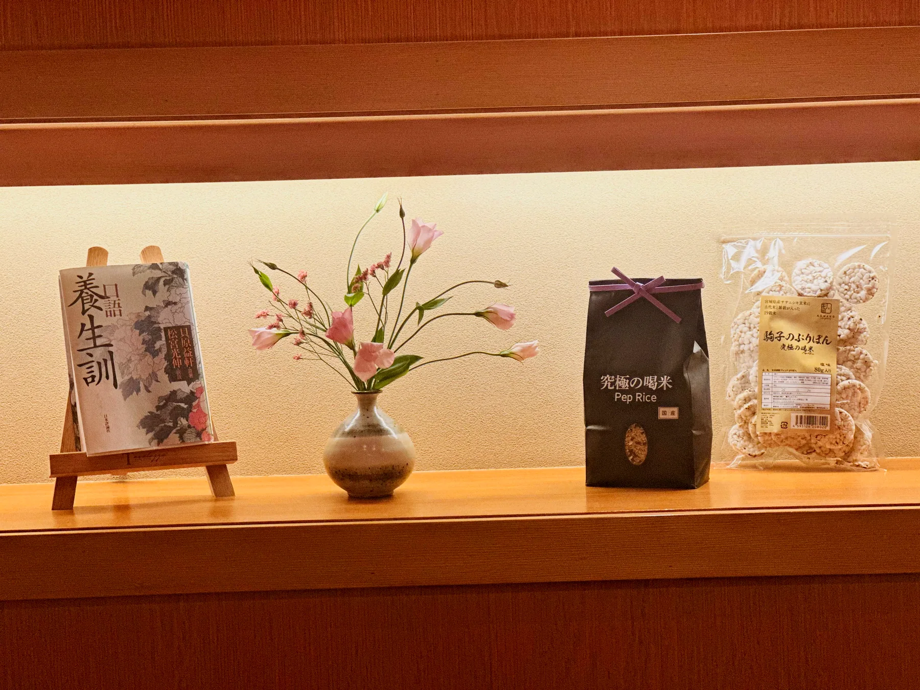 店の飾り棚。養生訓の本、季節の花、究極の喝米、駒子のぶりぽん
